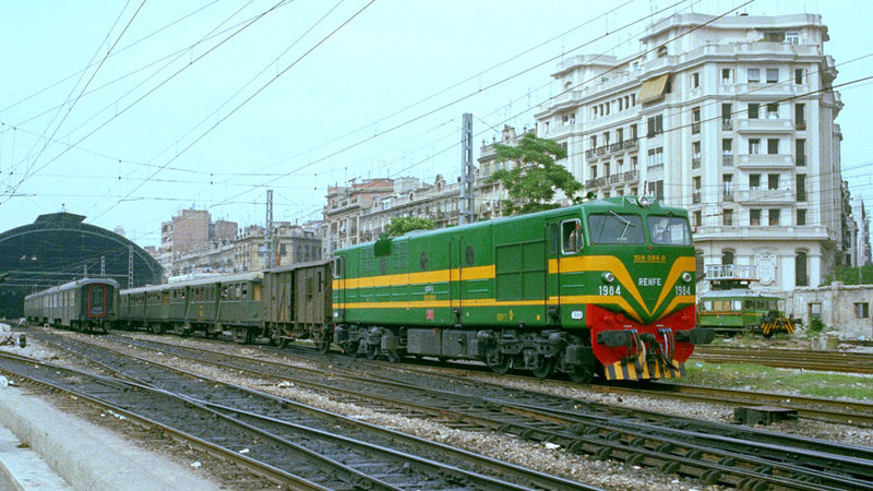 d129 319-084 en un original verde, con un cercanías a Gandía. Tras el DV, tres remolques tipo Geathom del año 1935, muy pesados para su automotor. Valencia Término, junio de 1976.jpg